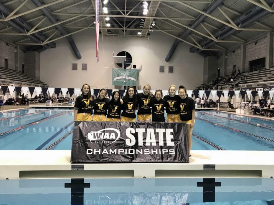 From left to right, freshman Madelyn Brown, freshman Grace Liu, freshman Jewel Hau, senior Julia Pakkala, freshman Naomi Voeller, freshman Megan Chow, sophomore Ella Marzec and junior Maddy Chow pose in front of the state championships banner prior to swimming at the preliminaries on Nov. 9.