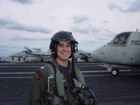 Patrick Myrick stands in front of a jet in his flight gear.