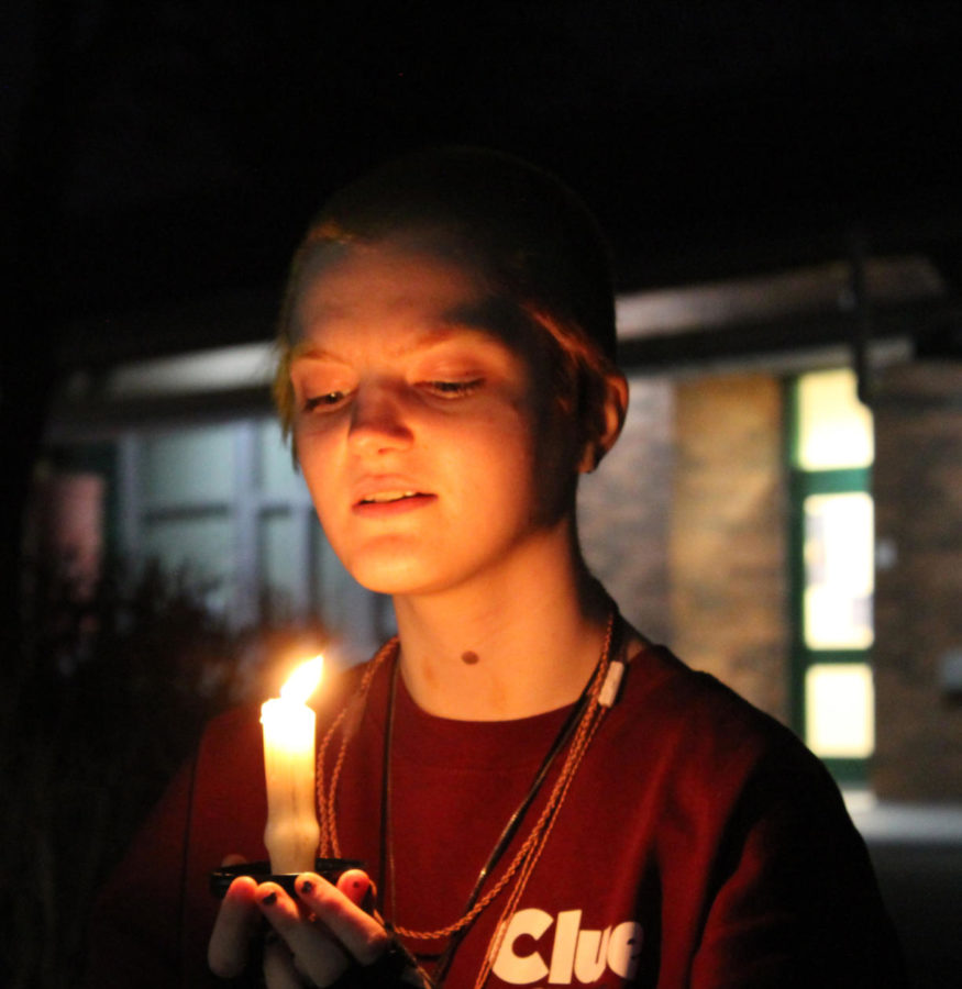 Senior Sky Darkhand holding a lit candle in the courtyard by the 100 building.
