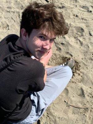 Senior Connor Foley, sitting on the beach looking up at senior Jacob Sims. 