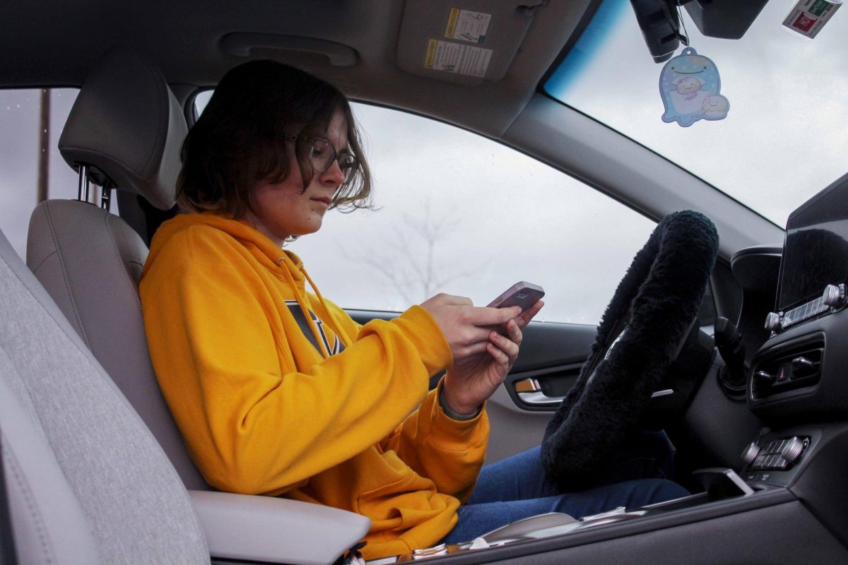 Martins poses with a phone in the driver's seat of their car, demonstrating what to avoid when driving. The vehicle was turned off for the purpose of this photo. 