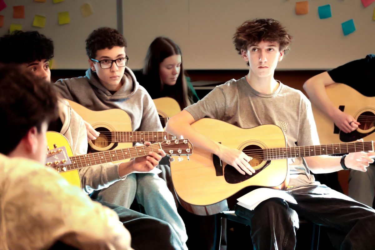 Students in guitar class practice newly learned chords. Many are trying to familiarize themselves with finger positions and sight reading music.