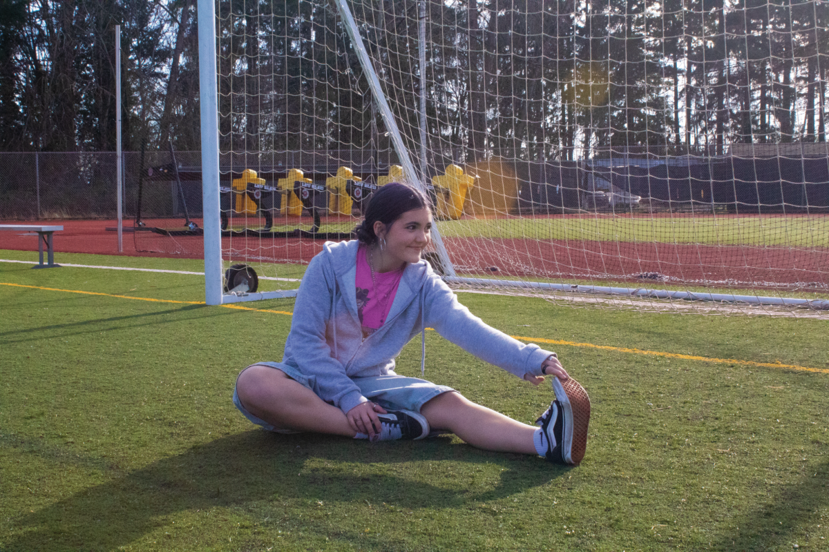Harris sits on the soccer field while stretching her ankle. This helps her restore mobility in her ankle and lowers the risk of re-injuring the same area.